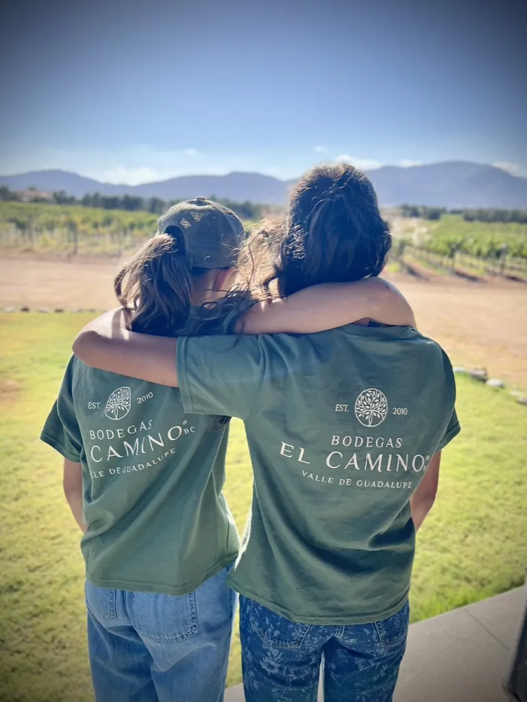 Dos jóvenes con camisetas de Bodegas El Camino frente al viñedo